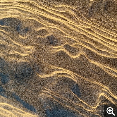 Macro shot of natural beige ridges in a sand dune. Dark blue shadows contrast against the highlights.